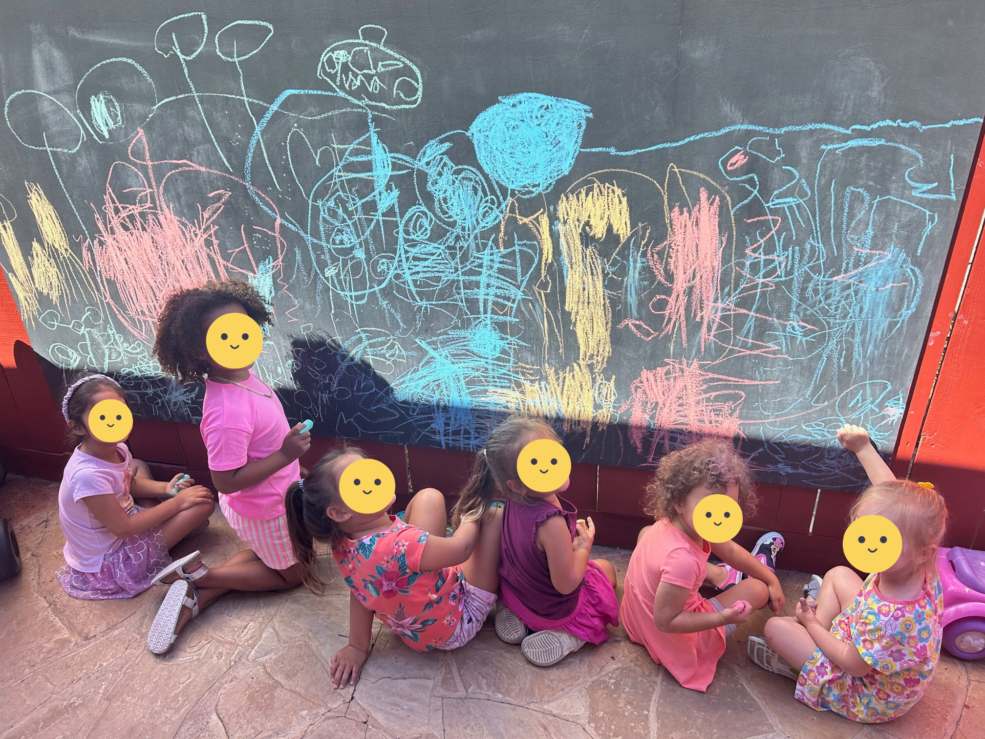 Children drawing on a blackboard outside.